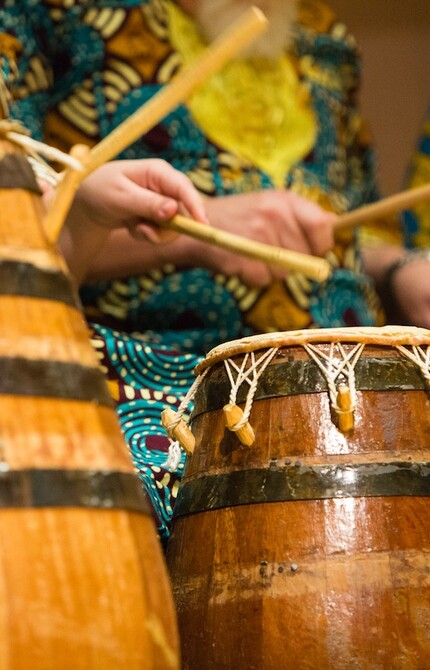Group dressed in traditional African clothing playing drums with sticks, creating music.
