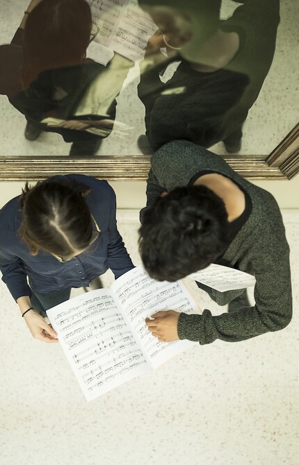 Overhead photo of two students reading a music score in front of a mirror.