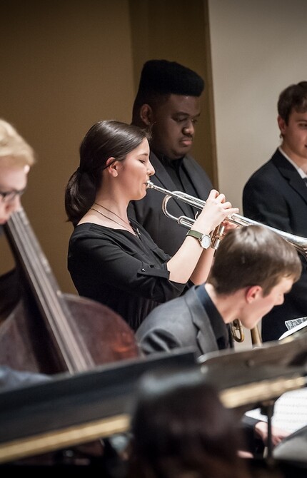 Trumpet player performing a solo while sitting in an ensemble, focused on their sheet music and instrument.