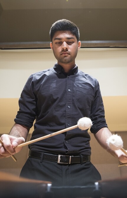 Percussionist wearing all black playing the marimba with four mallets, captured from the perspective of the marimba.