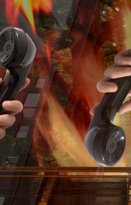 Two hands Holding telephones in front of an edited backdrop of of buildings, trees and fire
