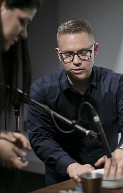 Two people surrounded by microphones, creating sound effects by manipulating a bowl of water, capturing the unique and creative sounds.