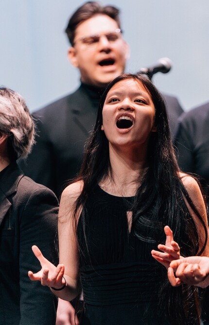 Choir performing on stage in performance attire, emotionally singing into microphones, with expressions of passion and focus.