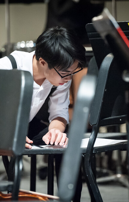 Young male kneeling down and looking at his music sheets on the chair