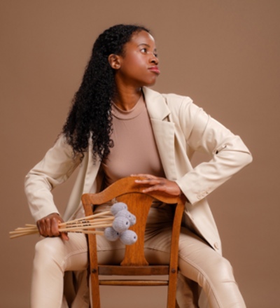 Person sitting backwards on a chair, wearing a beige suit, holding a bunch of mallets, with a relaxed yet focused expression.