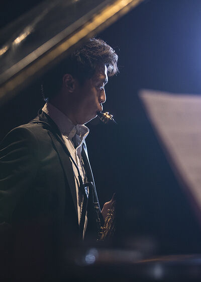 Saxophonist performing, seen from side through open piano lid