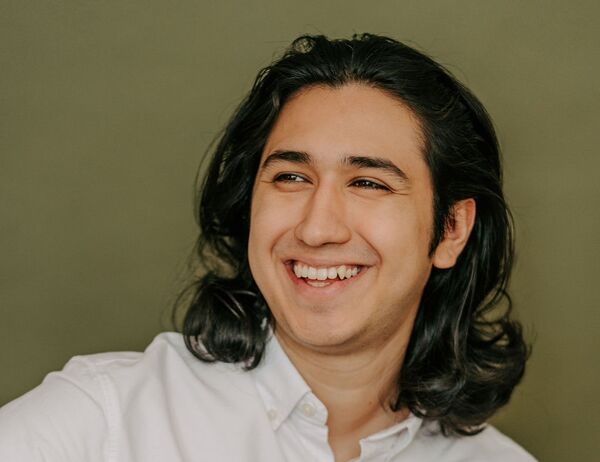 Man with long hair wearing a white dress shirt, smiling against a plain background.