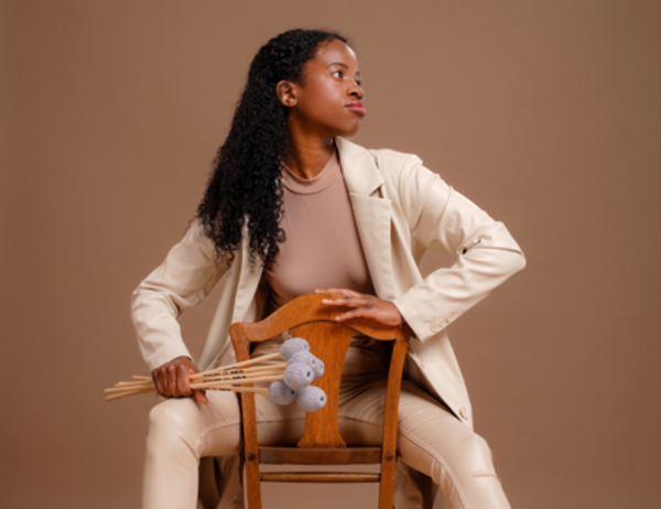 Person sitting backwards on a chair, wearing a beige suit, holding a bunch of mallets, with a relaxed yet focused expression.