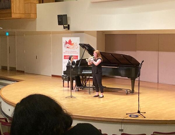 Trumpet player performing on stage with an accompanist on a grand piano, captured from the audience perspective.