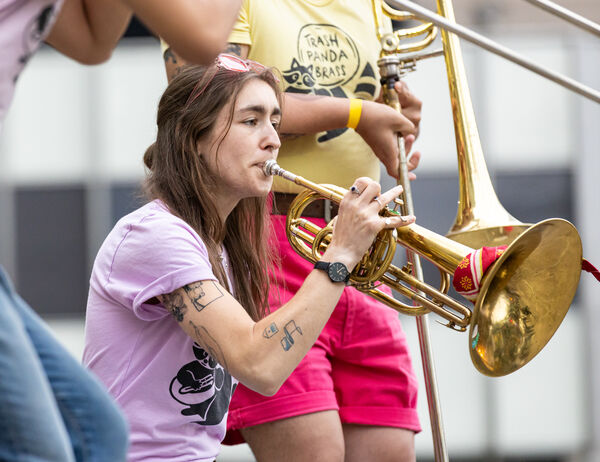 Person in a purple shirt playing a mellophone outdoors, standing beside others in colorful clothing, each playing their instruments.