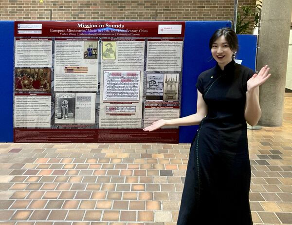 Person wearing a black dress presenting an information board in a tiled lobby, standing confidently.
