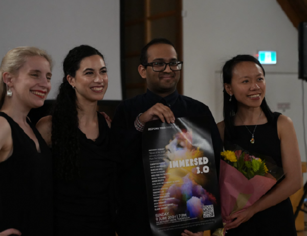 Group photo in a performance space, with one person holding a concert poster, surrounded by others smiling and posing together.