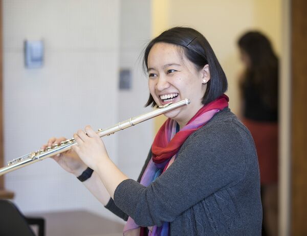 Person wearing a colorful scarf, smiling warmly while playing the flute.