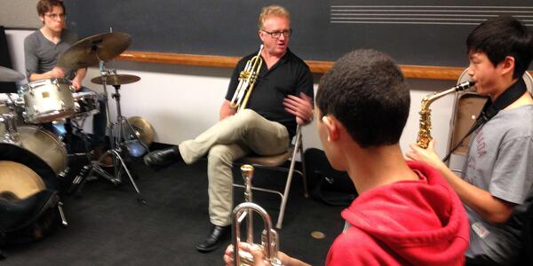 Jim Lewis holding trumpet and coaching student on saxophone.