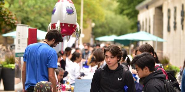 Students at an outdoor clubs fair talking at a table.