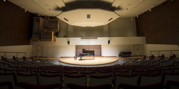 Empty performance hall with a grand piano placed on the stage, highlighting the spaciousness of the venue.