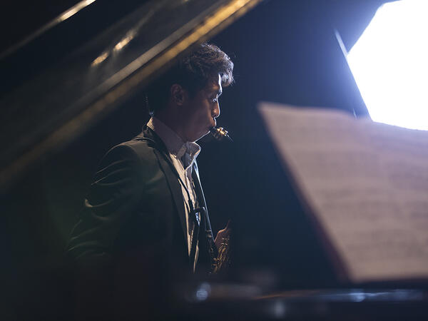 Saxophonist performing, seen from side through open piano lid