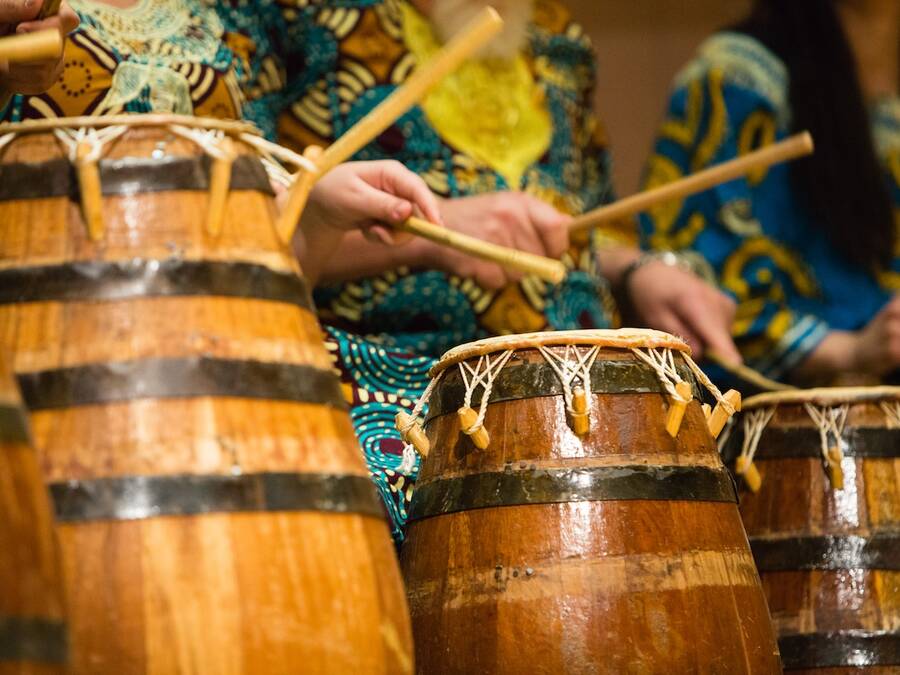 Group dressed in traditional African clothing playing drums with sticks, creating music. 