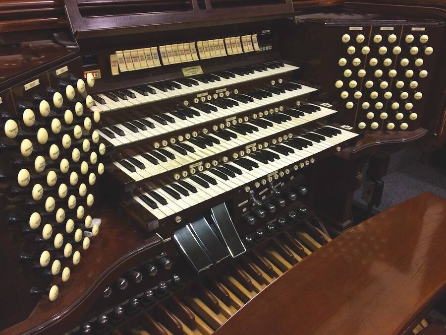Close-up view of a dark wood organ, focusing on the keyboard, pedals, and knobs, showcasing its intricate design and craftsmanship.