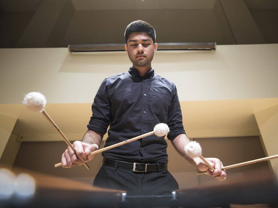 Percussionist wearing all black playing the marimba with four mallets, captured from the perspective of the marimba.