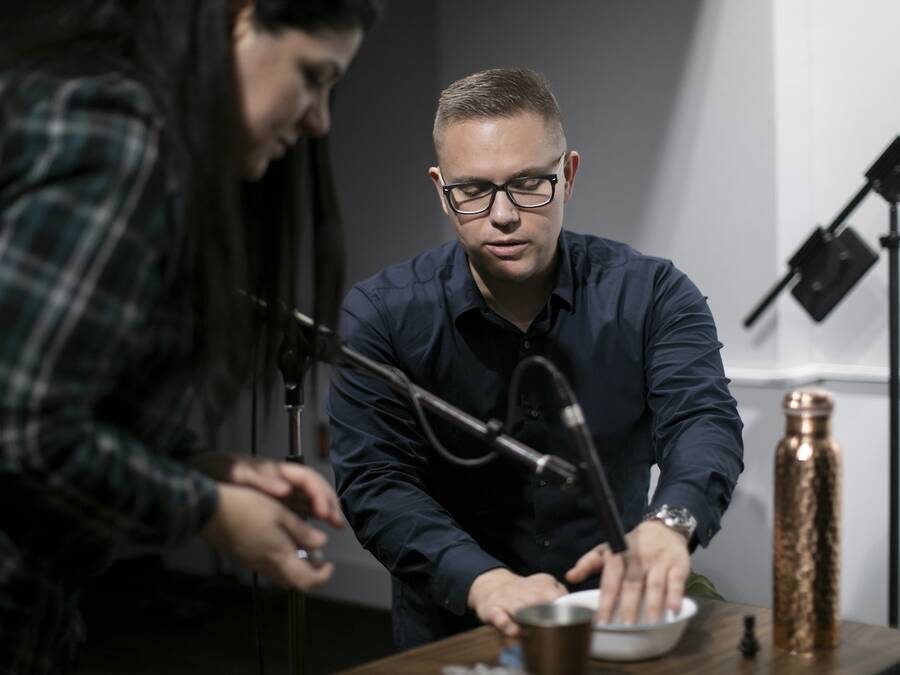 Two people surrounded by microphones, creating sound effects by manipulating a bowl of water, capturing the unique and creative sounds.