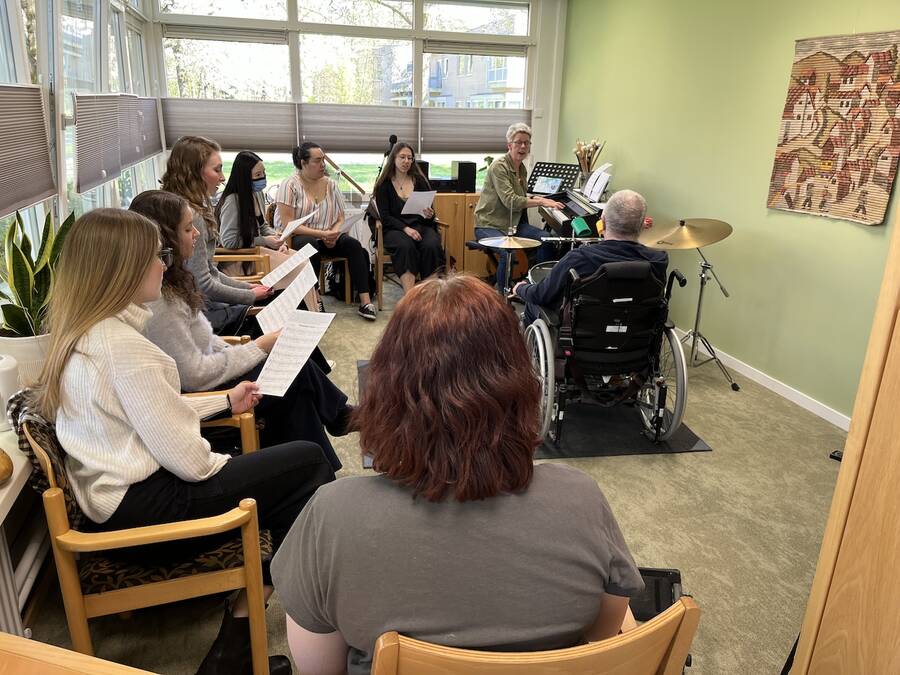 Man in a wheelchair and a piano accompanist facilitating a music class, with students engaged in the lesson.