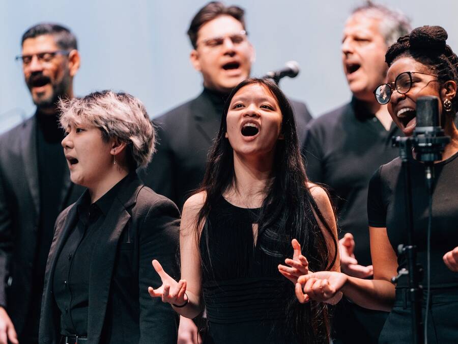 Choir performing on stage in performance attire, emotionally singing into microphones, with expressions of passion and focus.
