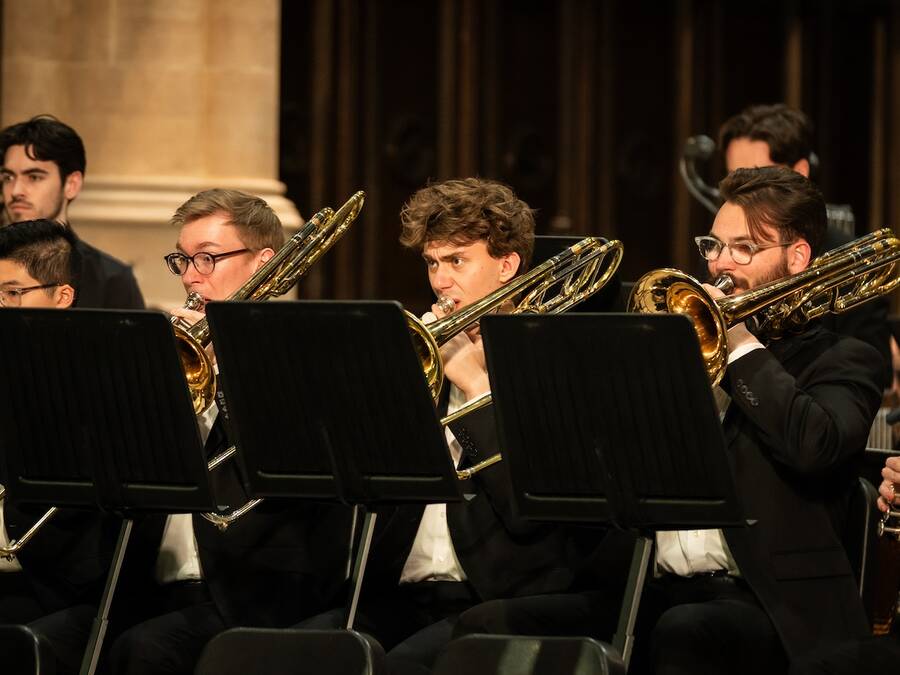 Trombone section of an ensemble standing while performing, each musician focused and playing in unison, contributing to the overall sound of the group.