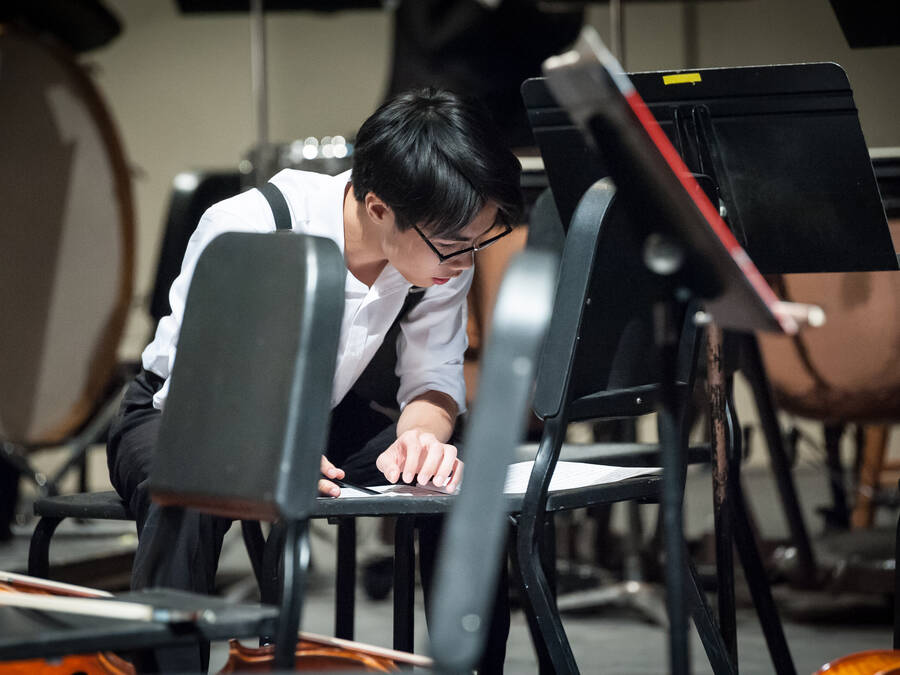 Young male kneeling down and looking at his music sheets on the chair