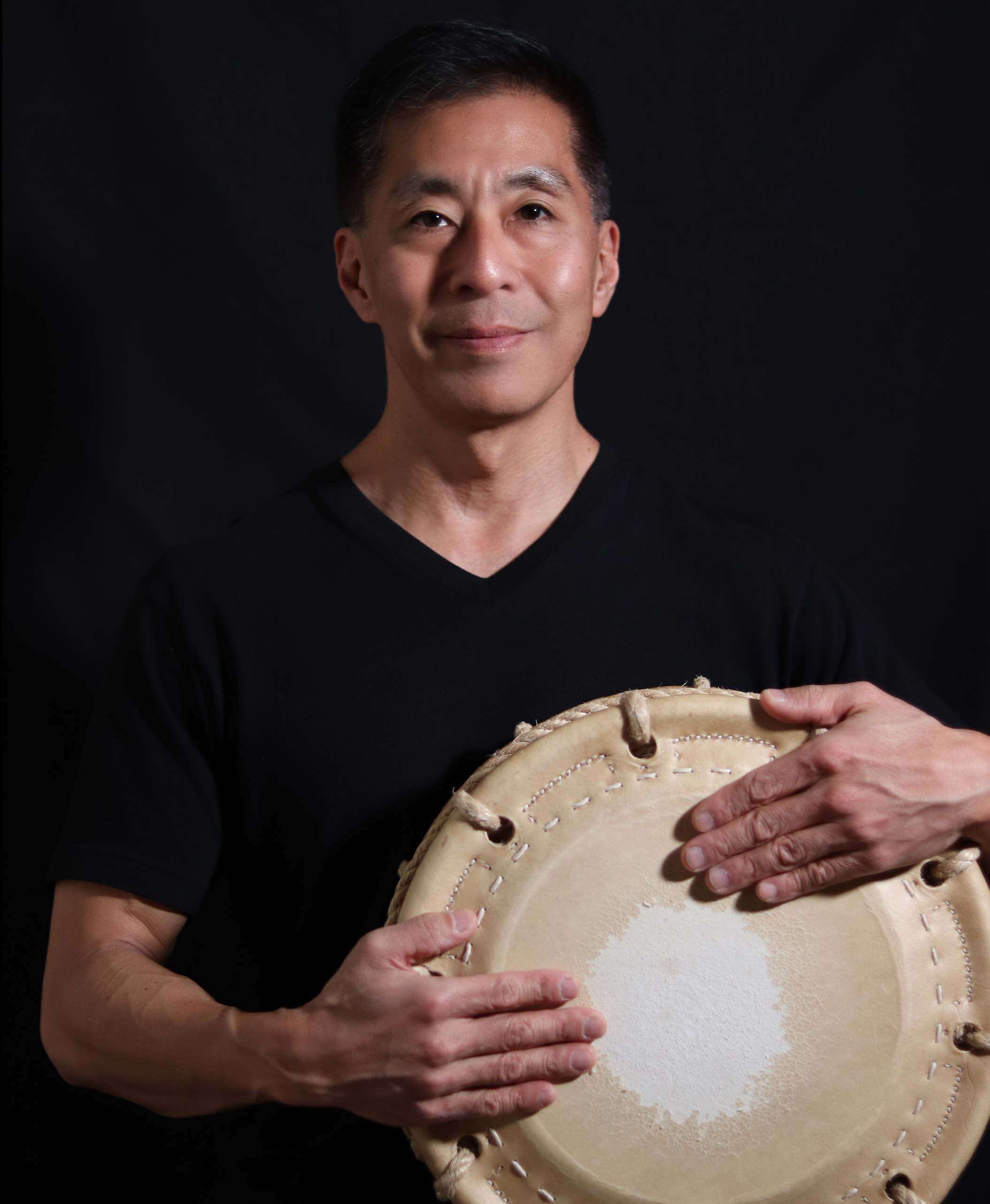 Professional headshot portrait of Kiyoshi Nagata against a black backdrop holding his drum