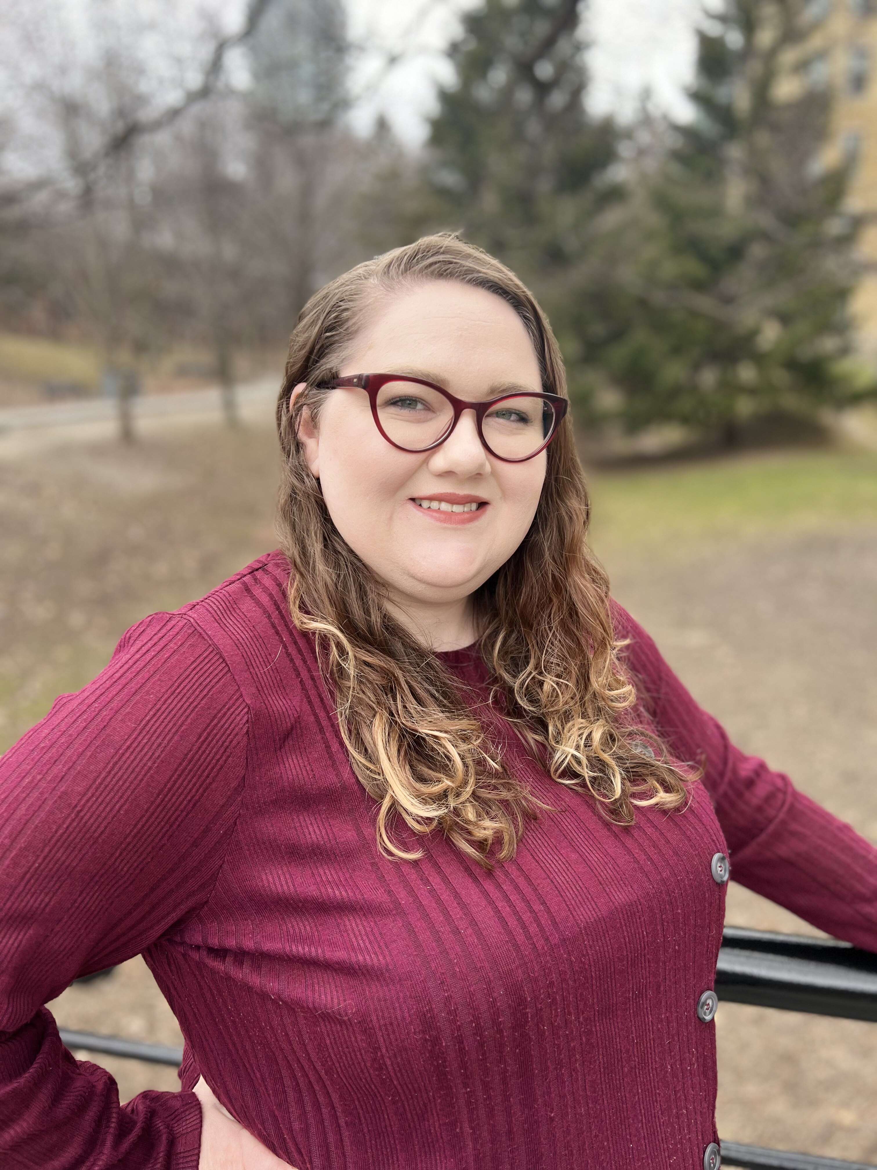 Portrait of Taryn Dougall wearing a red top, leaning against a rail against a park background.
