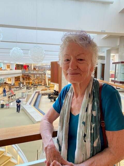 Photo of an older person wearing a blue shirt and a scarf, standing on the balcony of a museum.