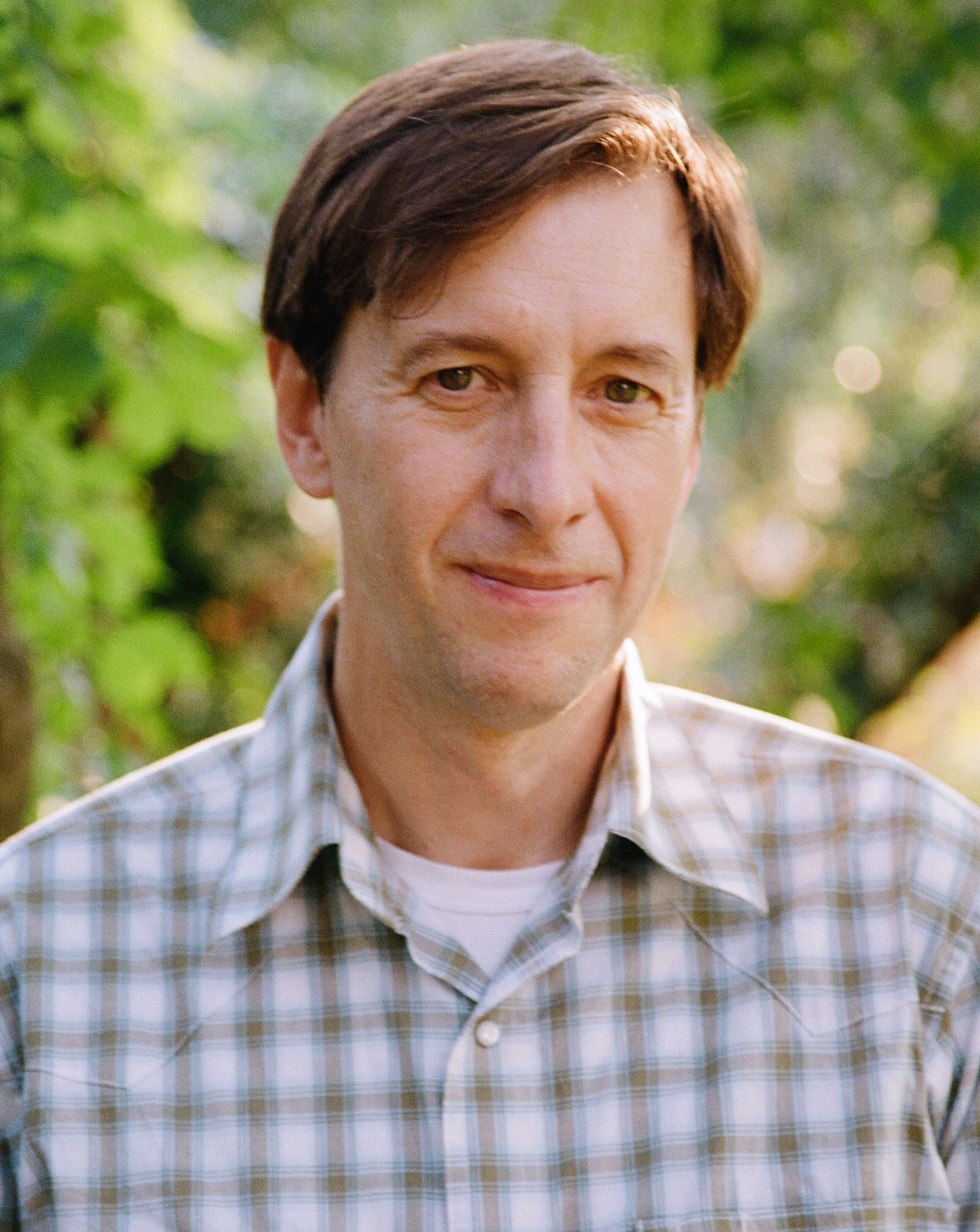 Peter Johnston poses in front of a faded backdrop of trees.