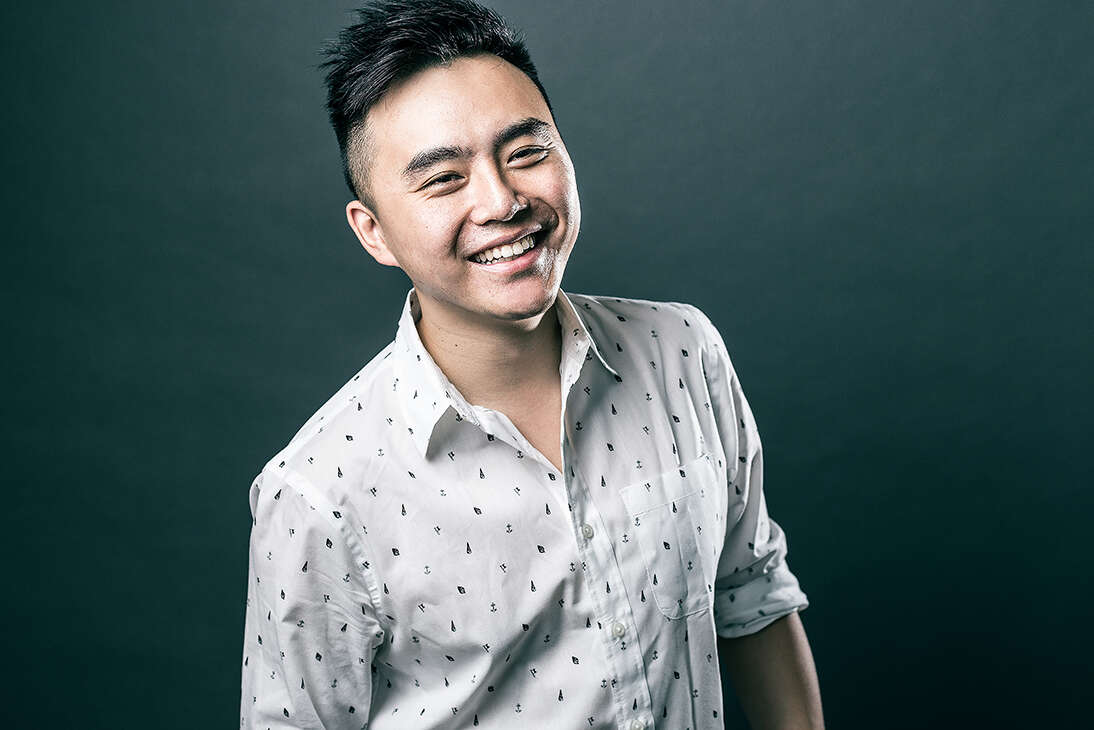 Man wearing a white dress shirt, smiling in front of a dark background. 