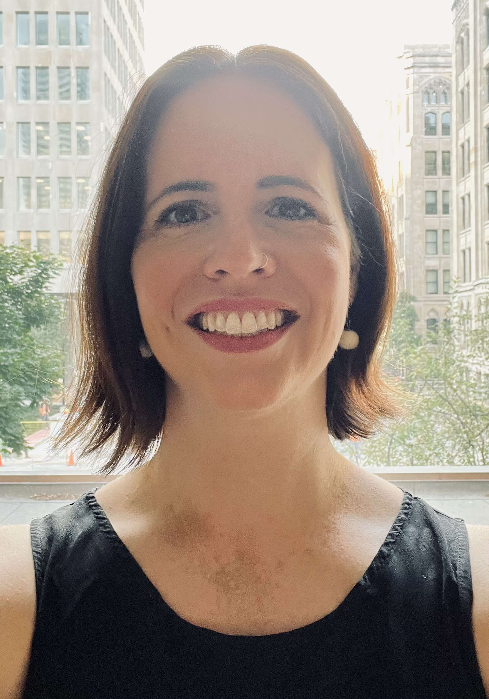 Headshot of a woman wearing a black shirt, smiling in front of a window with a city street in the background.
