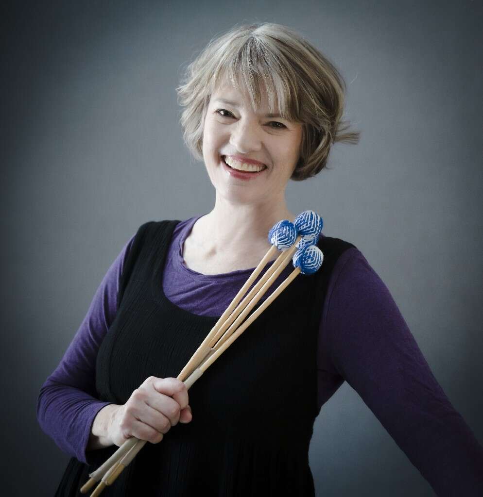 Person with short hair, wearing a purple and black dress, holding percussion mallets.