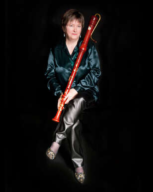 Person sitting with their legs crossed, wearing dark-colored satin, holding a bassoon.