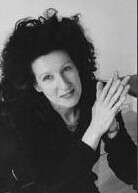 Black and white photo of a person with big hair, wearing a black shirt, holding their hands in a praying position