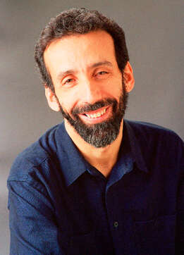 Headshot of a person with a beard, wearing a navy button-down shirt in front of a grey background.