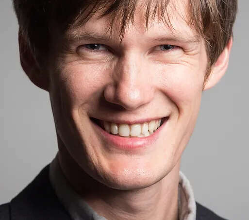 headshot of person with blue eyes, wearing a suit, smiling warmly.