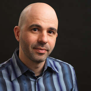 Bald person wearing a blue striped shirt, looking at the camera with a dark background, creating a focused and confident look.