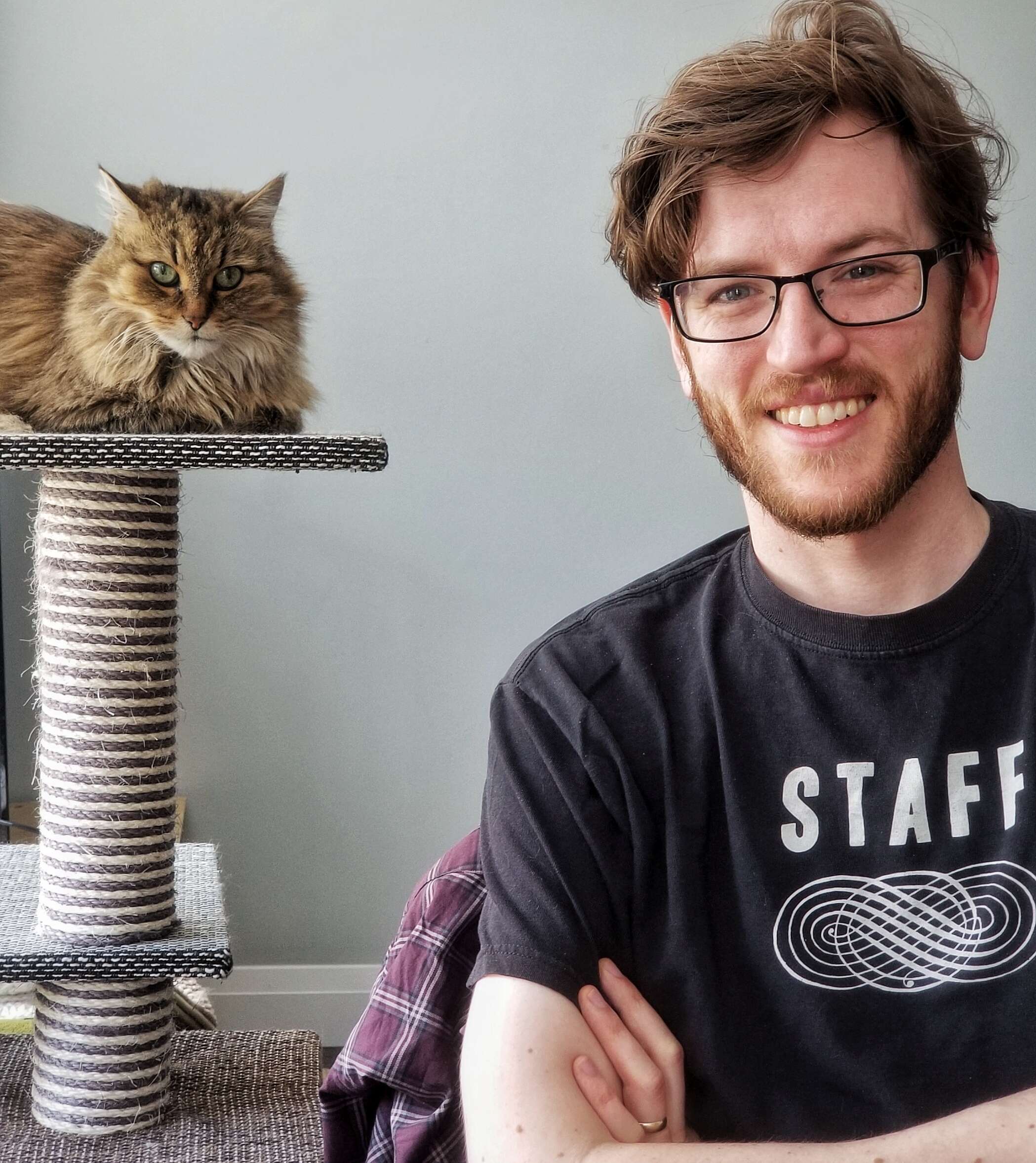 Picture of Colin Harris sitting down, arms crossed, smiling, with cat in the background.