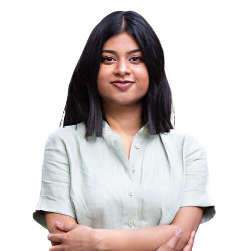 Headshot of a person with shoulder-length hair, wearing a grey shirt, standing in front of a white background, with a neutral or friendly expression.