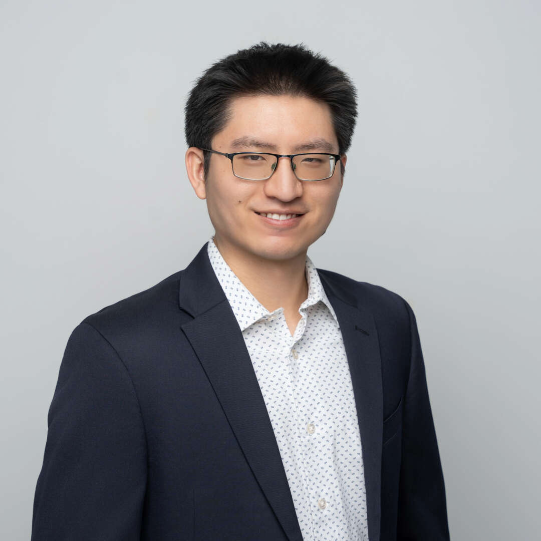 Man wearing glasses and a blazer in front of a white background