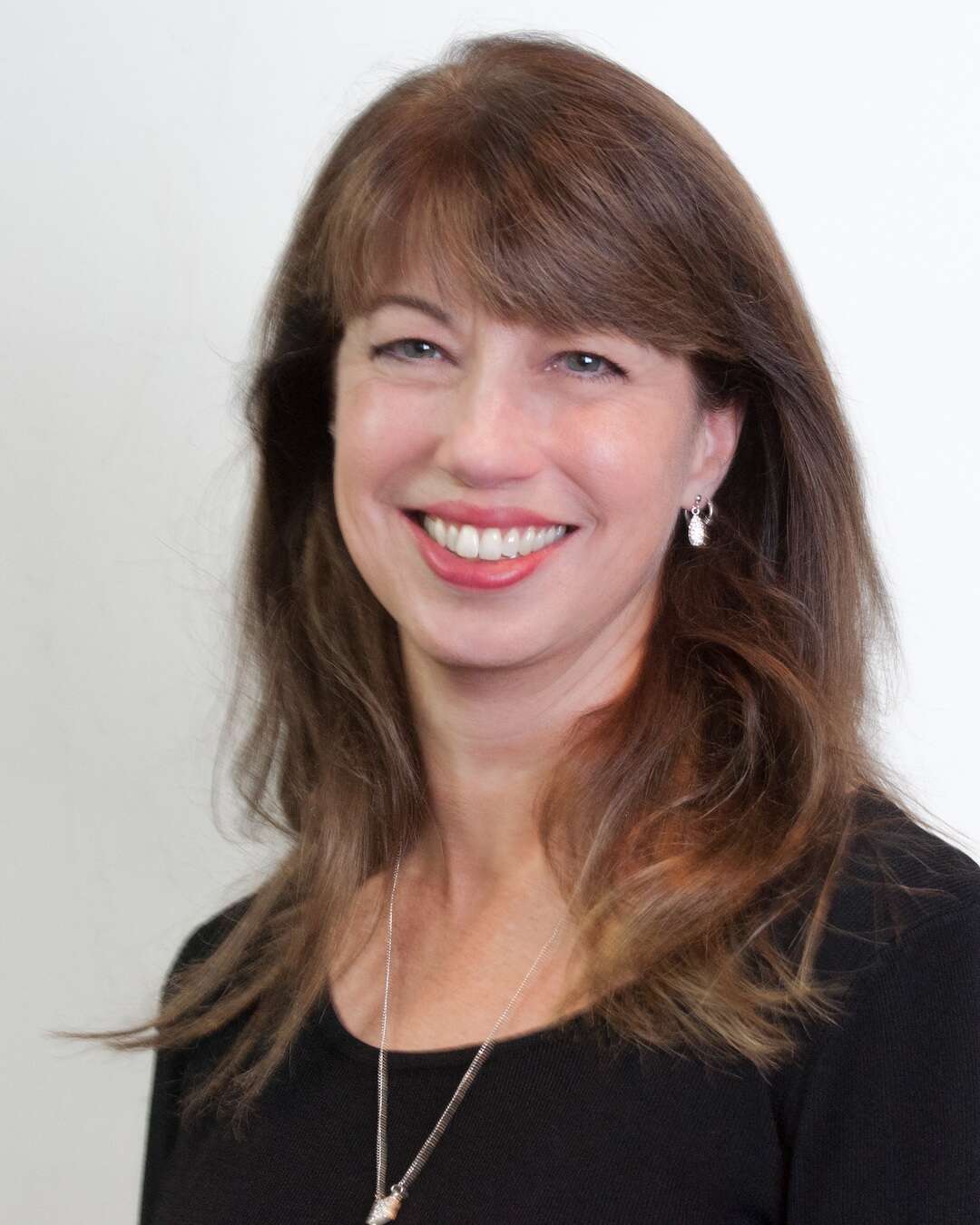 Headshot of a person with shoulder-length hair and bangs, smiling while wearing a black shirt