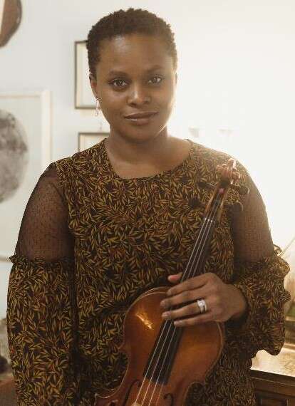 A person wearing a black patterned blouse is holding a violin.
