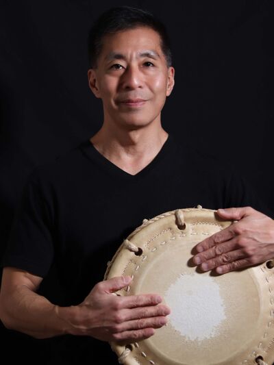 Professional headshot portrait of Kiyoshi Nagata against a black backdrop holding his drum