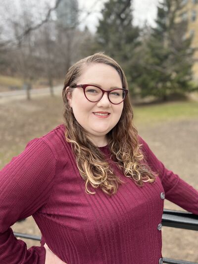 Portrait of Taryn Dougall wearing a red top, leaning against a rail against a park background.