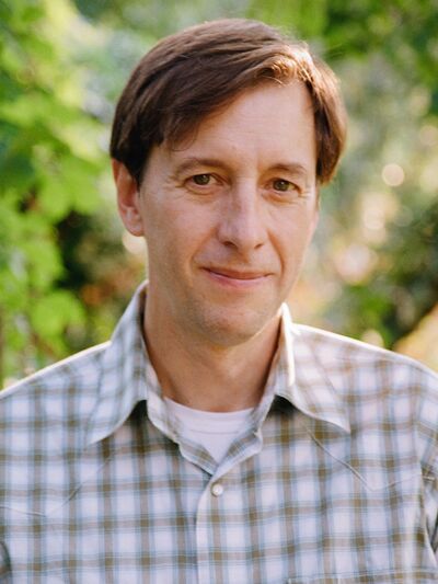 Peter Johnston poses in front of a faded backdrop of trees.
