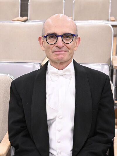 Close-up picture of John Rudolph sitting in the middle of a row of seats with a professional suit. 